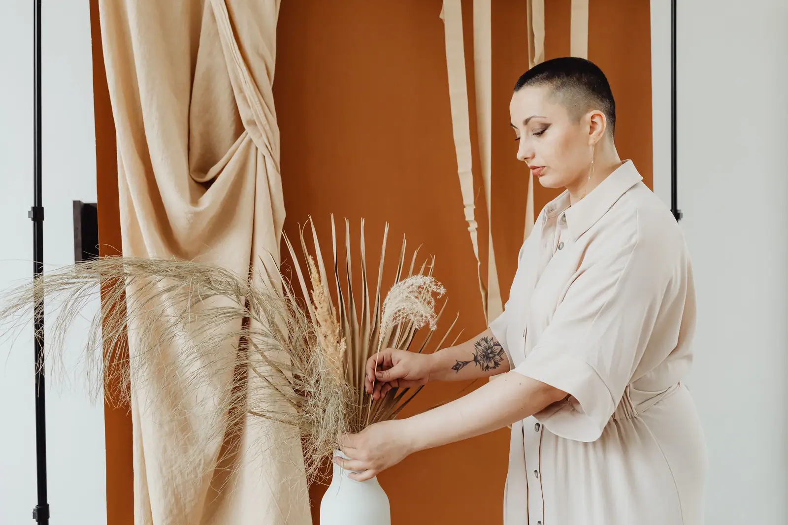 Romy Whitlock, a stylist with a buzzed head, arranging dried grasses in her clay-colored studio