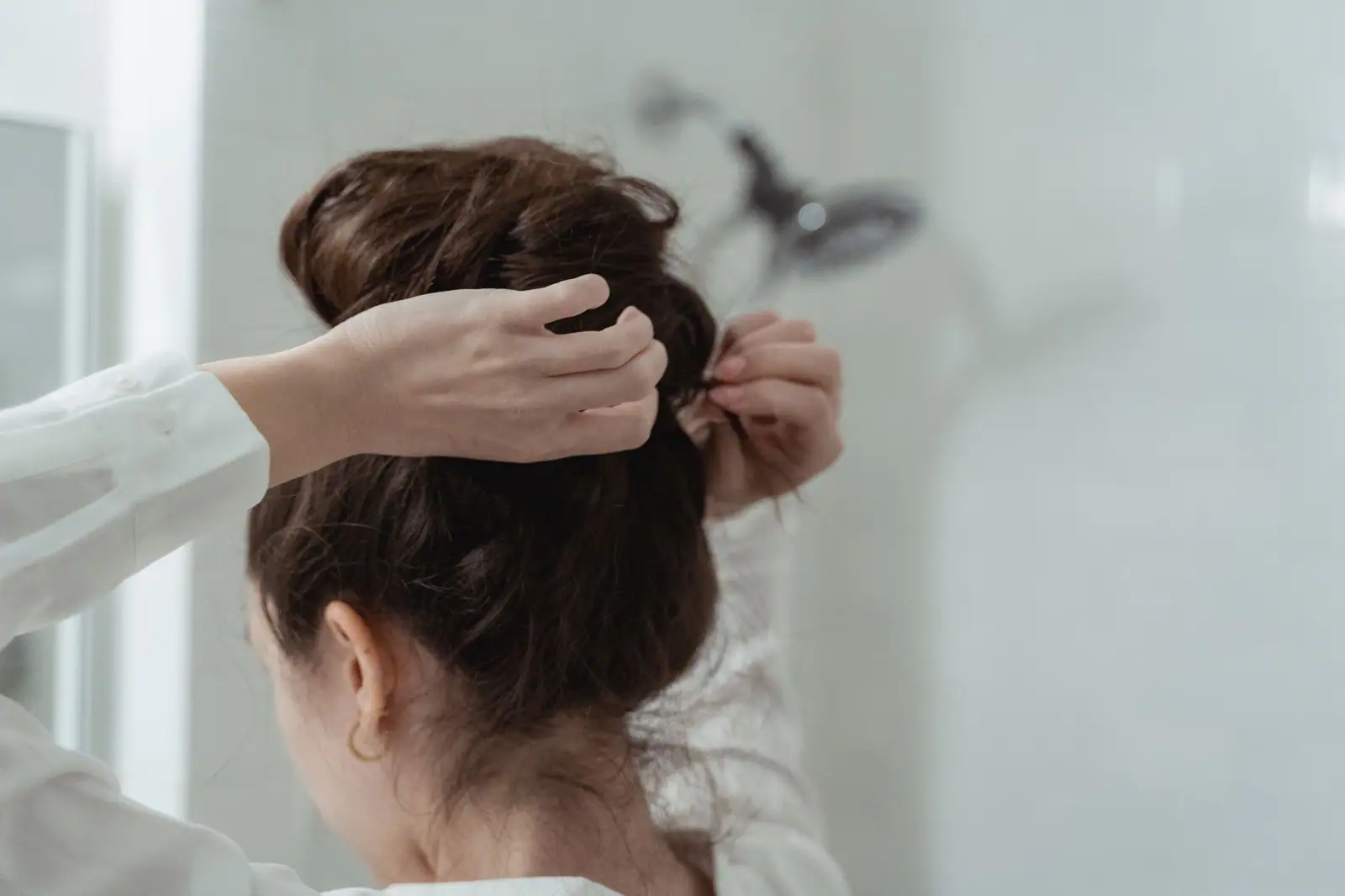 Hands pinning a soft brunette bun, seen from behind