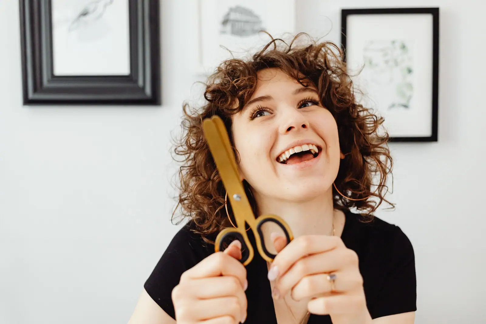 Goldie Marsh laughing and holding her gold shears in front of framed sketches