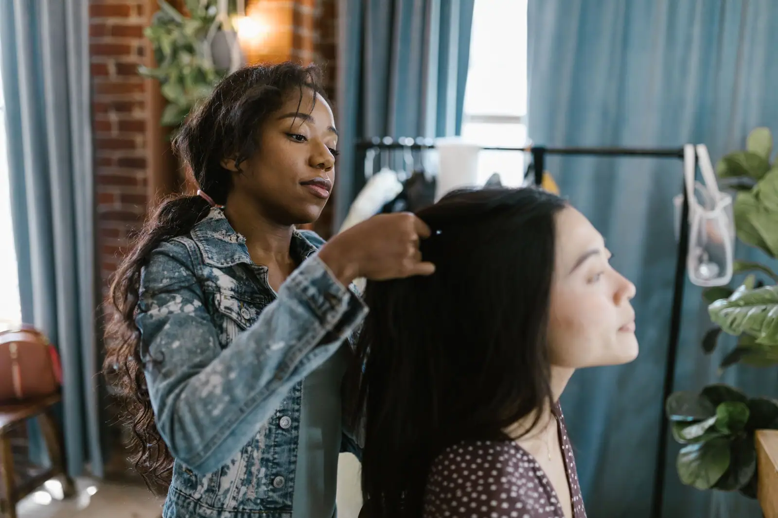 Tasha Monroe, in a denim jacket, adjusting a client's long black hair in her studio