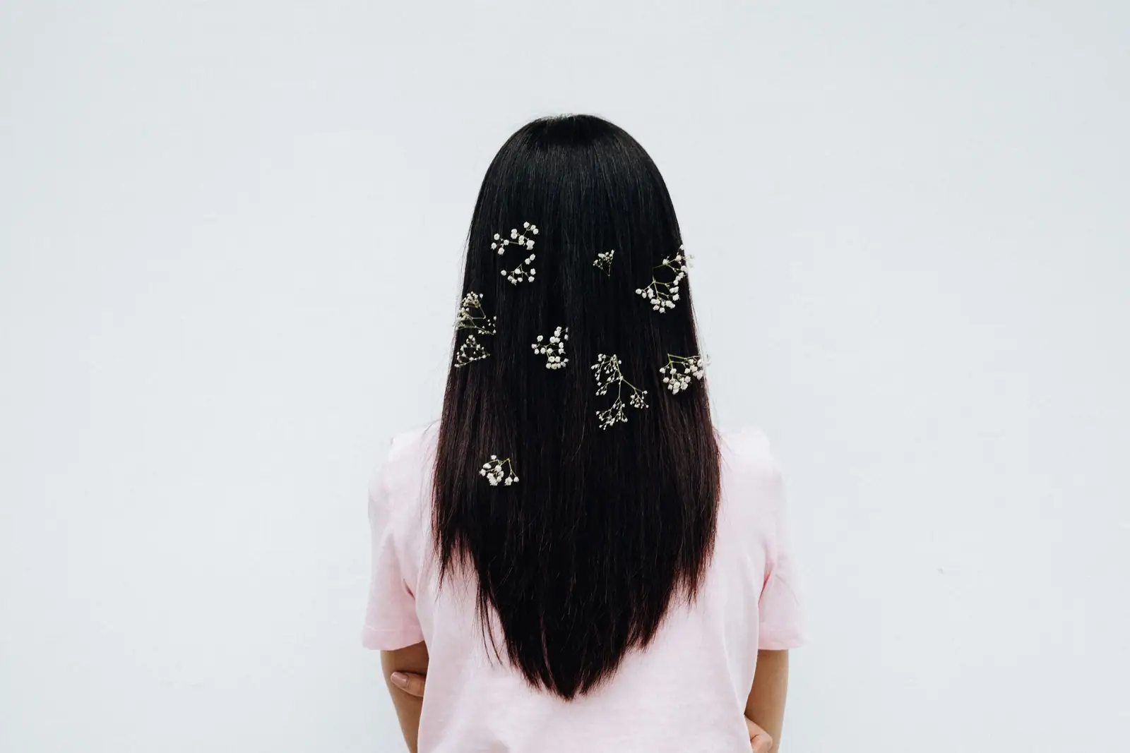 Long, thick, straight black hair seen from behind, dotted with sprigs of baby’s breath