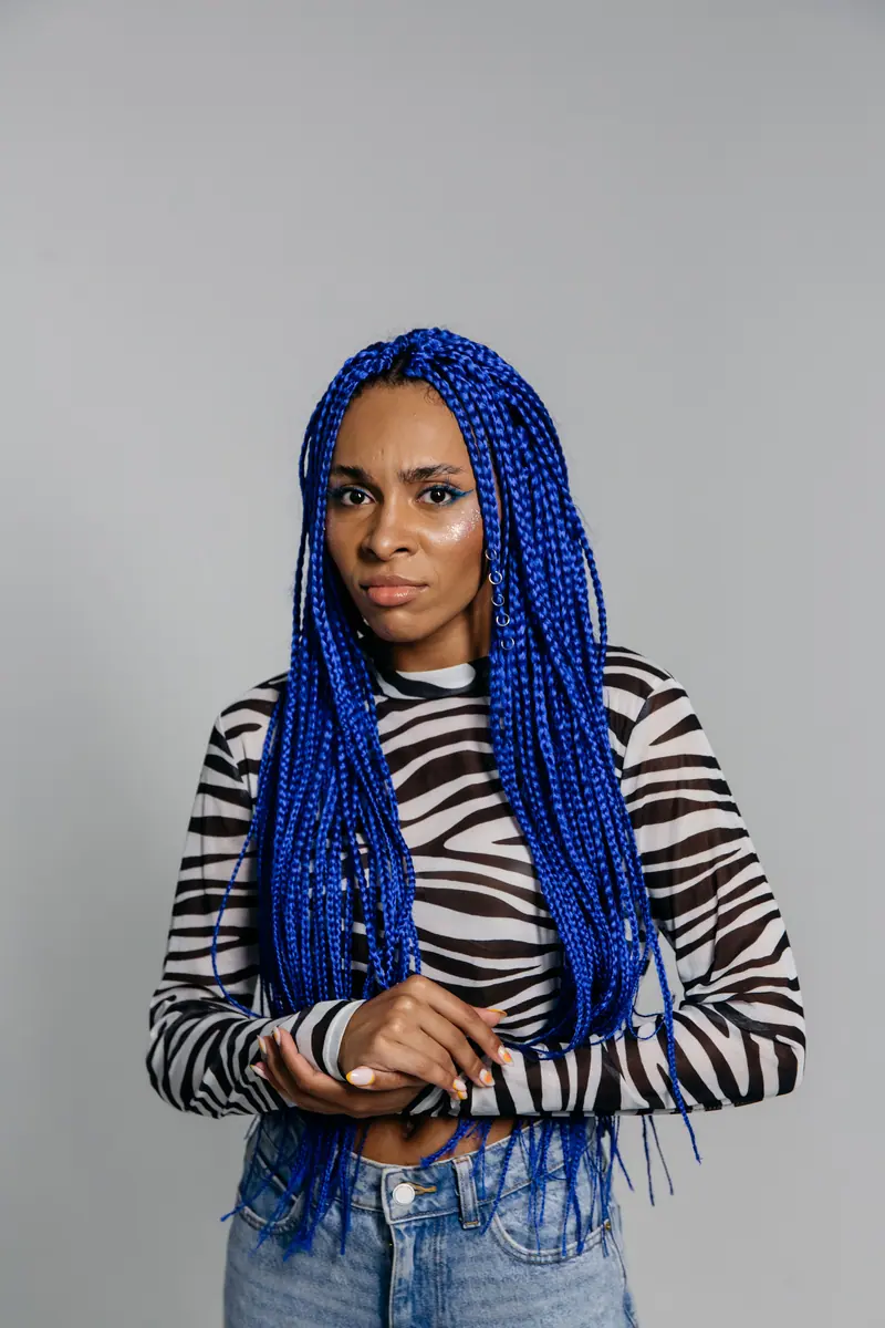 A woman with long blue braids and zebra print top posing in a studio setting.