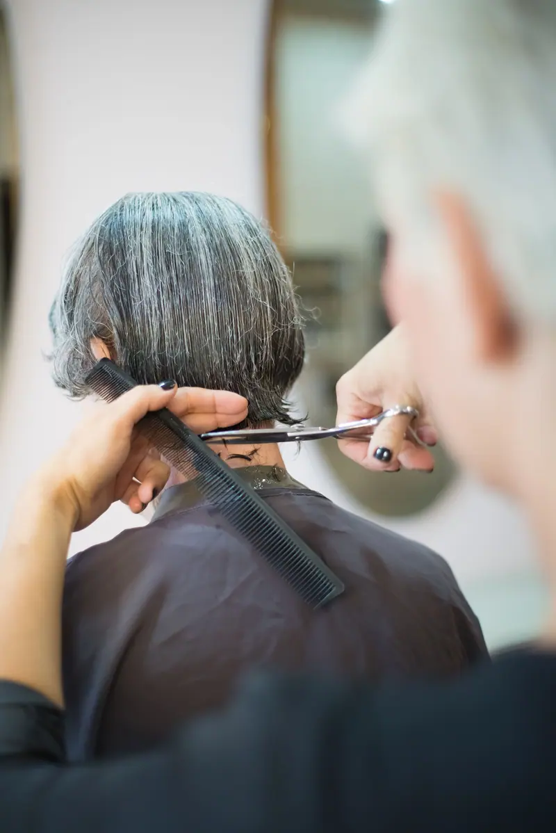 A hairstylist skillfully cutting a woman's hair with scissors and comb indoors.