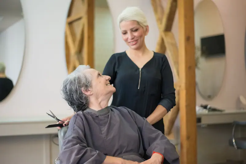 A happy senior woman enjoys her time at a hair salon with a friendly stylist.