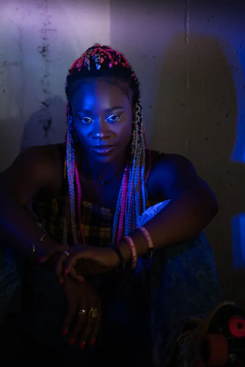 Vibrant, artistic portrait of a woman with braided hair in colorful lighting.