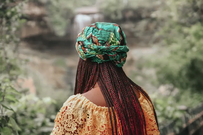 A woman with braided hair and headscarf enjoying the outdoors in a vibrant setting.