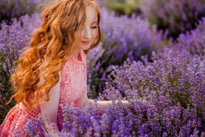 Red-haired woman in pink dress enjoying serene lavender field in daylight.