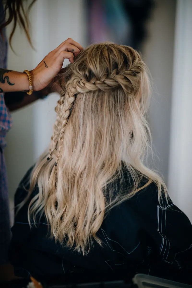 Detailed view of a hairstylist braiding a woman's blonde hair in a salon setting.