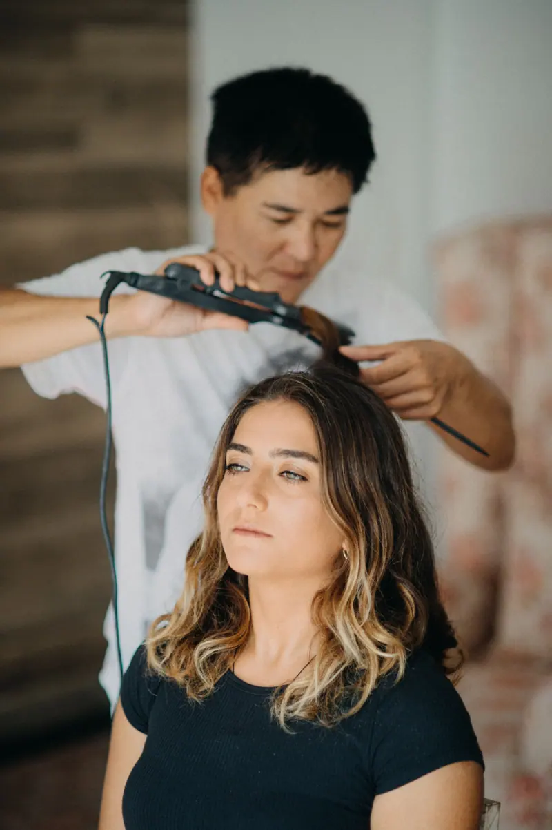 Hairdresser using curling iron on woman's wavy hair in salon.