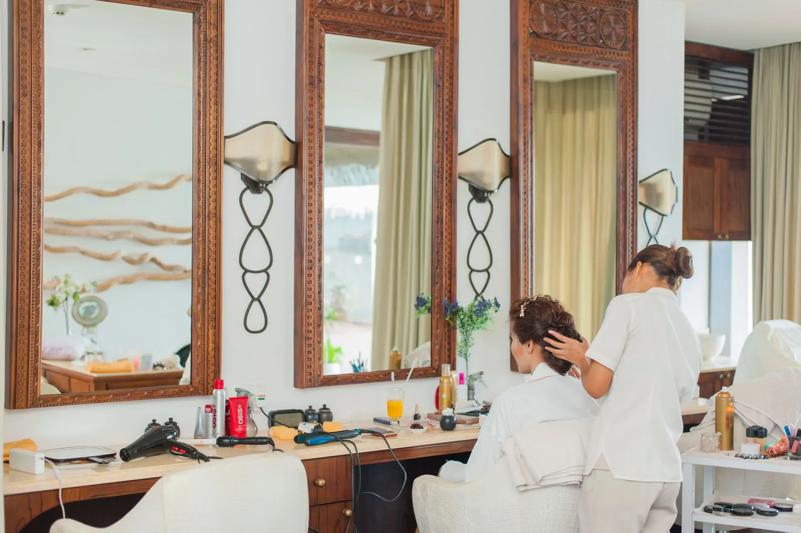 Stylists at work beneath tall carved-wood mirrors in a classic, sunlit salon