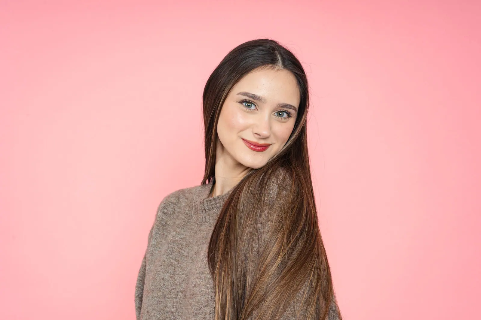 Smiling woman with long glossy brown hair against a bubblegum-pink wall