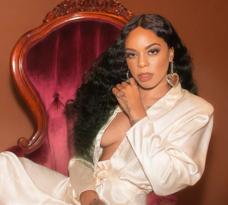 Elegant woman in satin robe posing stylishly on a vintage chair indoors.
