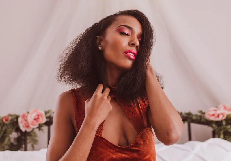 A confident woman poses gracefully in a boudoir setting with soft lighting and floral accents.
