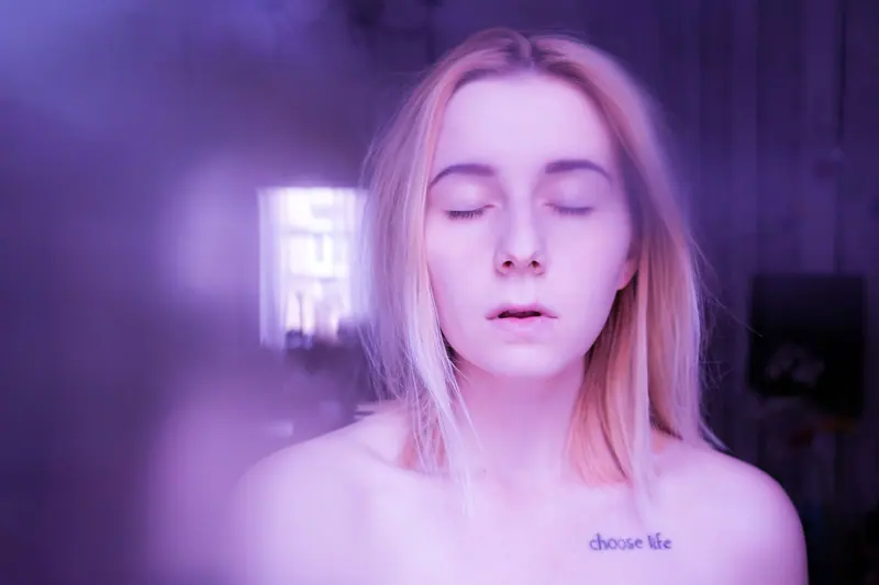 A serene portrait of a woman with closed eyes in a dreamy purple light.