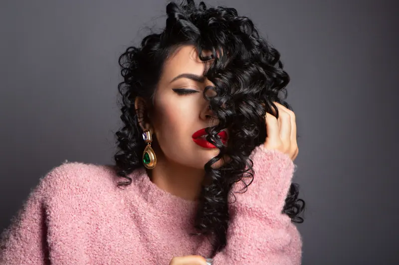 Portrait of an elegant woman with curly hair and bold red lips, eyes closed in contentment.
