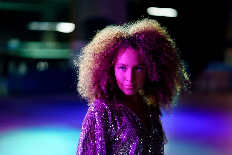 Stylish woman with curly hair shines under disco lights. Sequin outfit adds sparkle.