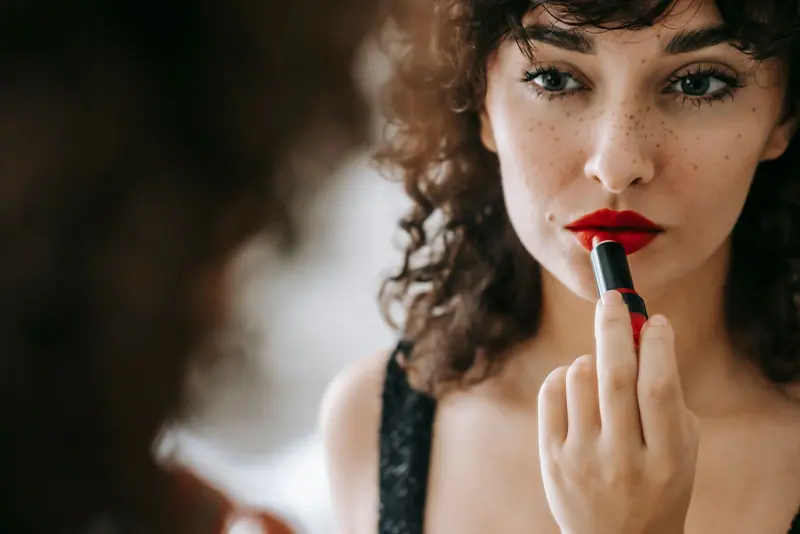 Close-up of a woman applying red lipstick while looking in a mirror. Elegant and confident beauty routine.