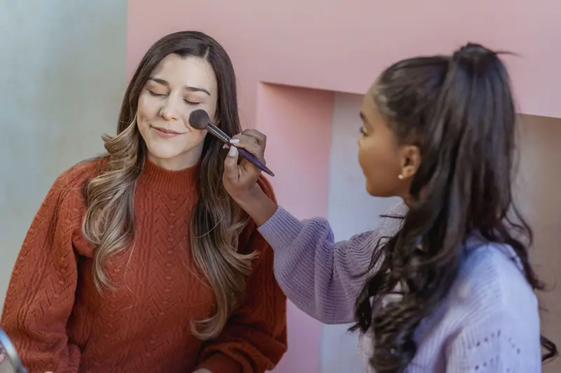 Two women applying makeup indoors, showcasing beauty and friendship in a modern setting.