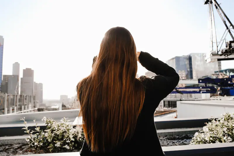 Rear view of a woman with long brown hair observing a city skyline. Bright and modern urban scene.