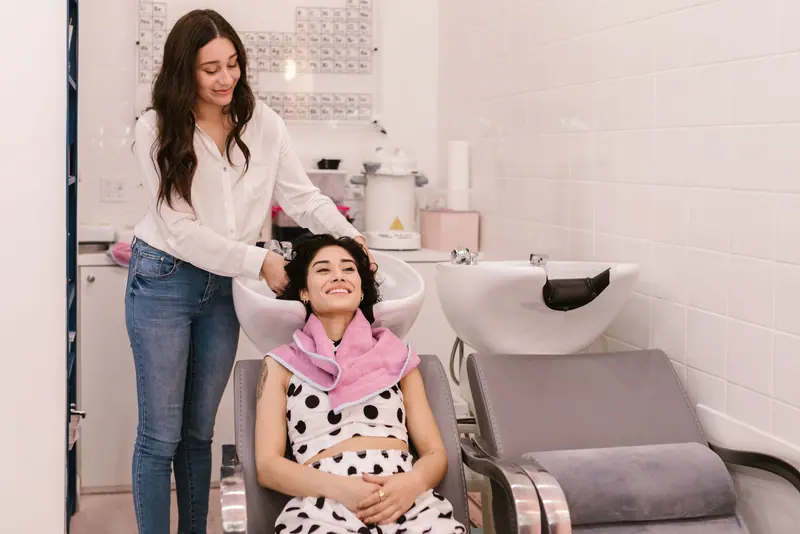 Two women in a hair salon enjoying a relaxing hair wash session, showcasing pampering and self-care.