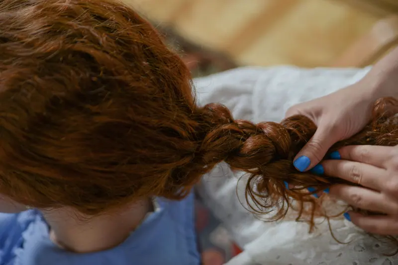 Close-up view of hands braiding red hair, showing hairstyle detail.
