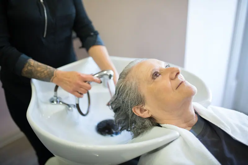 Senior woman getting hair washed by stylist in a cozy salon setting.