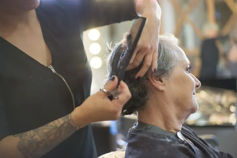 A hairdresser giving a stylish haircut to a senior woman in a warm and friendly salon environment.