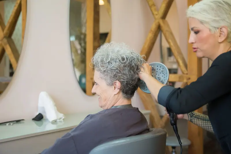 A hairdresser styling an elderly woman's hair in a salon, showcasing senior hair care.