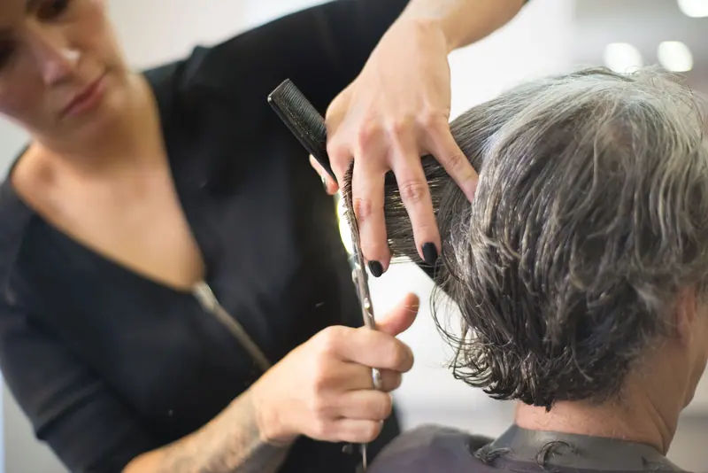 Hairdresser cutting senior woman's hair in a salon with close-up view of the hands and tools.