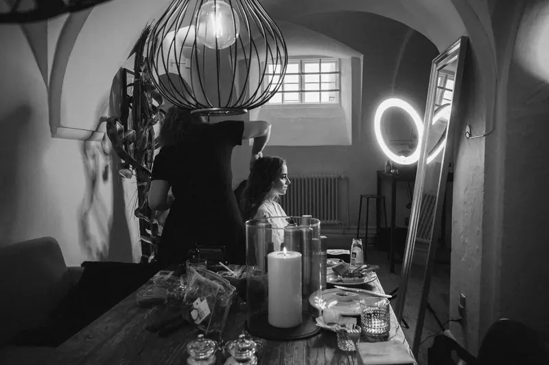 A hairdresser styles a woman's hair in a salon with ring lamp illumination.