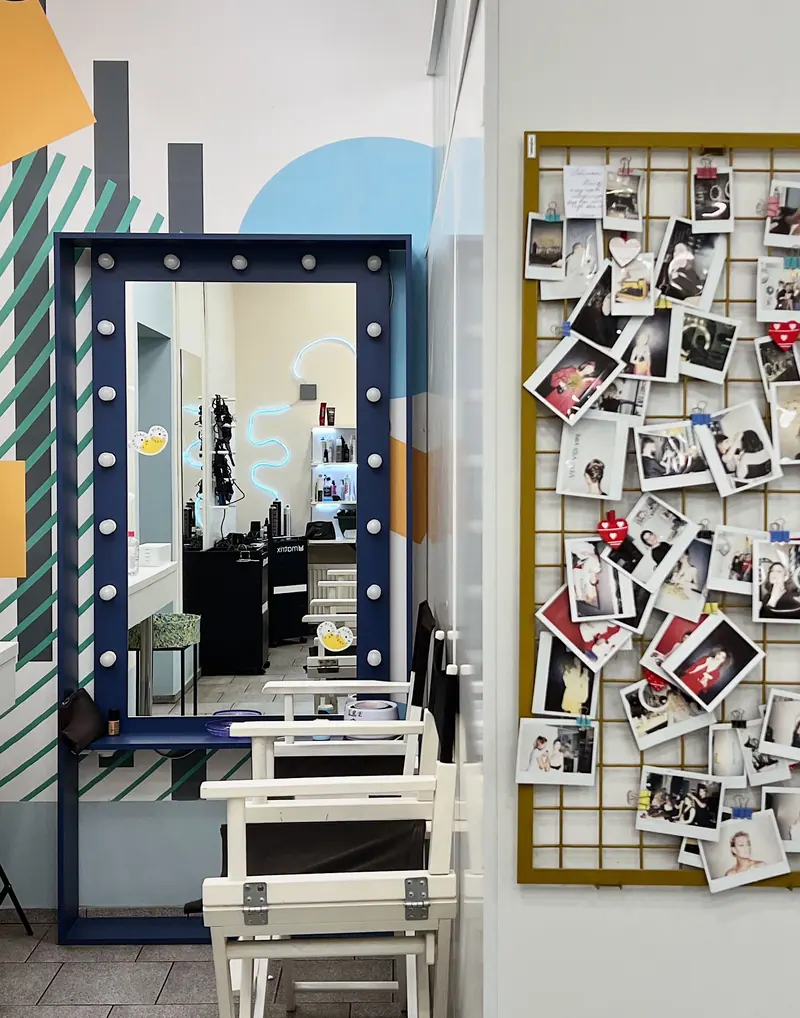 Colorful salon interior featuring a vanity mirror and a wall of polaroid photos, capturing artistic ambiance.
