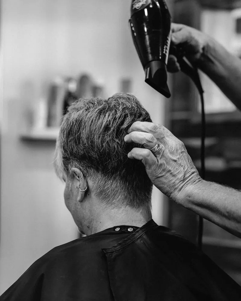 Grayscale image of a hairdryer in use at a hair salon, capturing the client's haircut in progress.