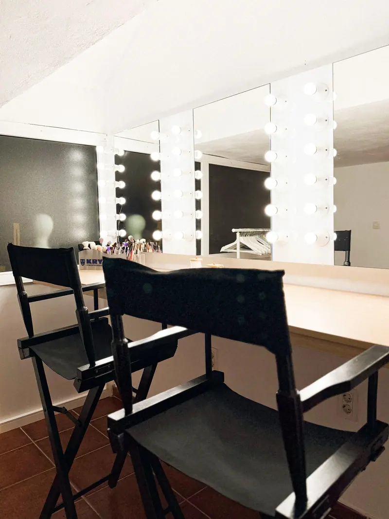 Bright, stylish makeup studio interior featuring illuminated vanity mirrors and director chairs.