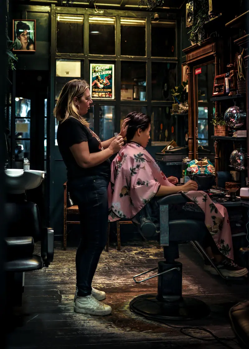 Stylist working at a single chair in a dark, plant-filled salon suite