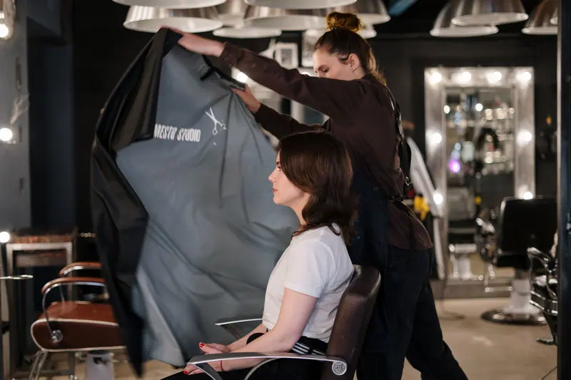 Hair stylist draping cape over client for a haircut in a modern hair salon setting.