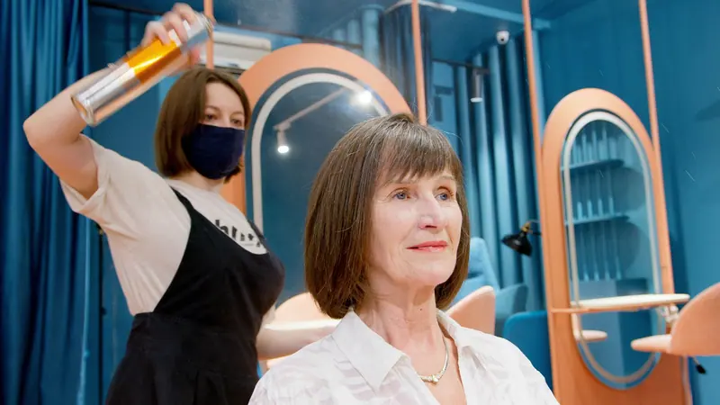 A hairstylist applies hairspray to a senior woman's new hairstyle in a modern salon.