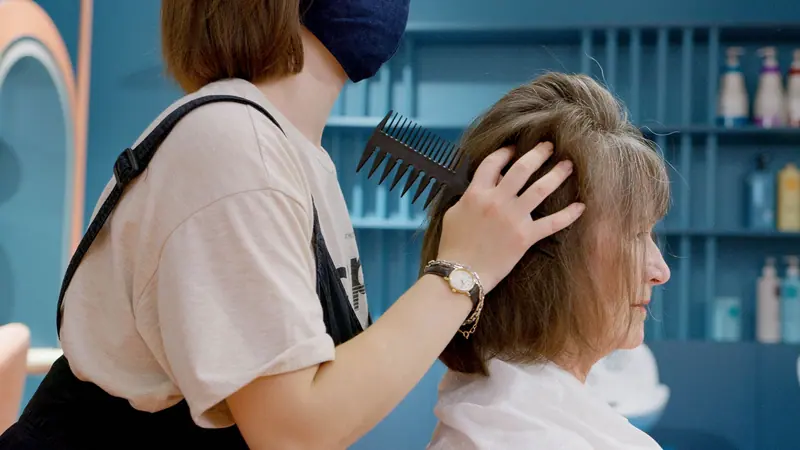 A hairstylist combing a senior woman's hair at an indoor salon, showcasing professional care.