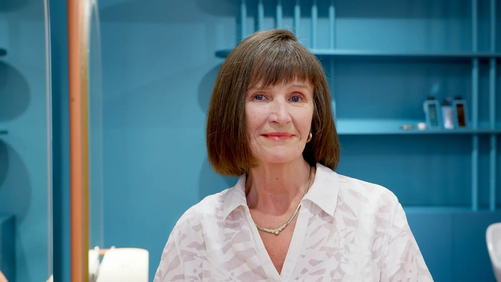 Smiling woman with a glossy brown bob in a teal-blue private salon suite