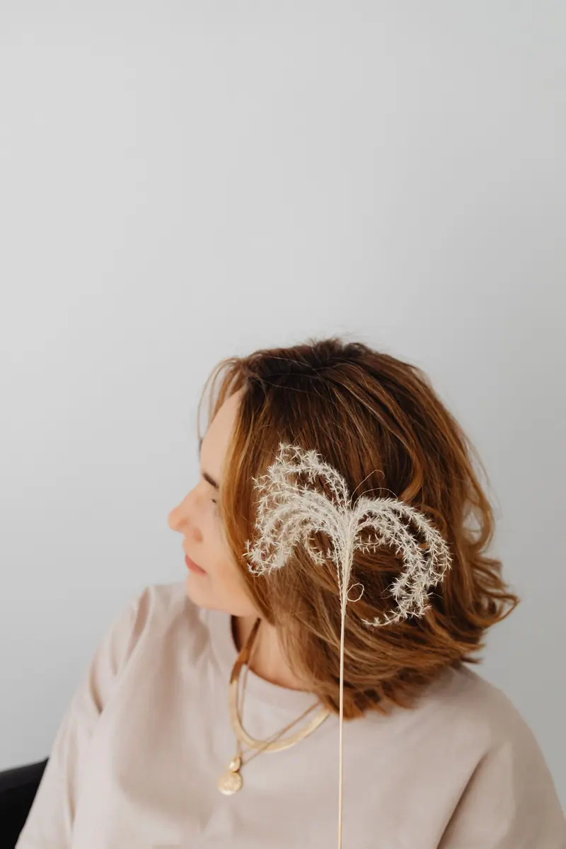 A serene portrait of a woman with a delicate floral hair accent against a gray background.