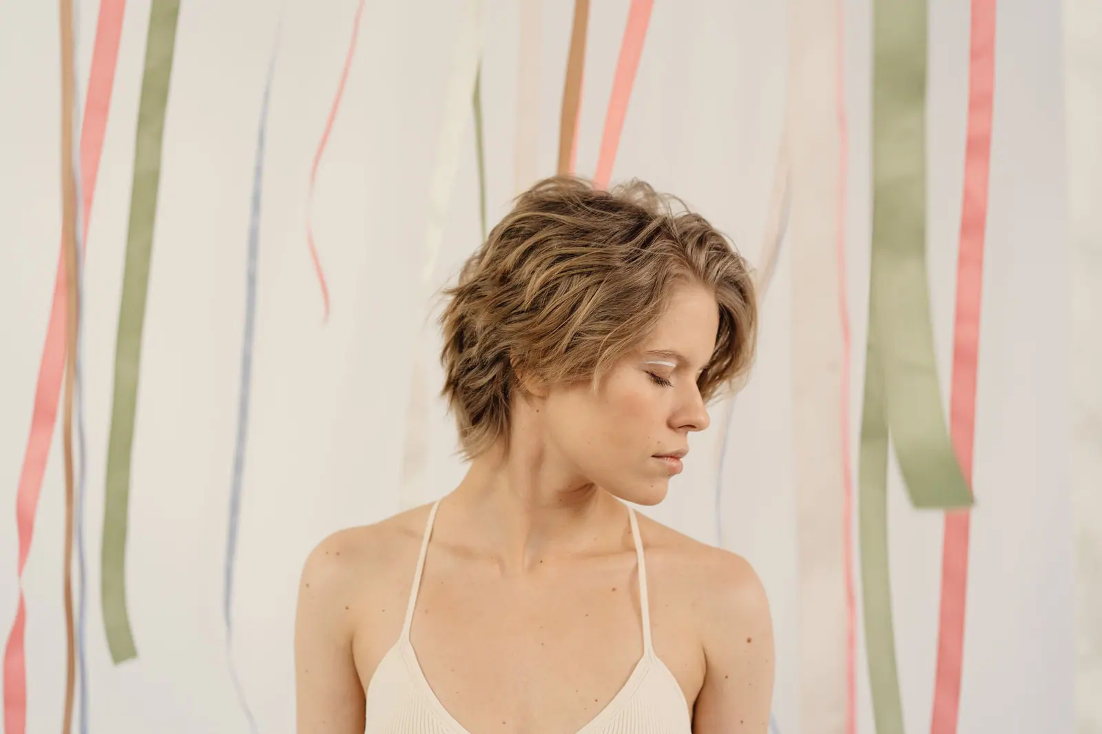 Woman with a soft tousled pixie cut standing beside hanging silk ribbons