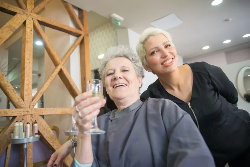 Stylist and smiling client toasting in a warm oak-framed suite