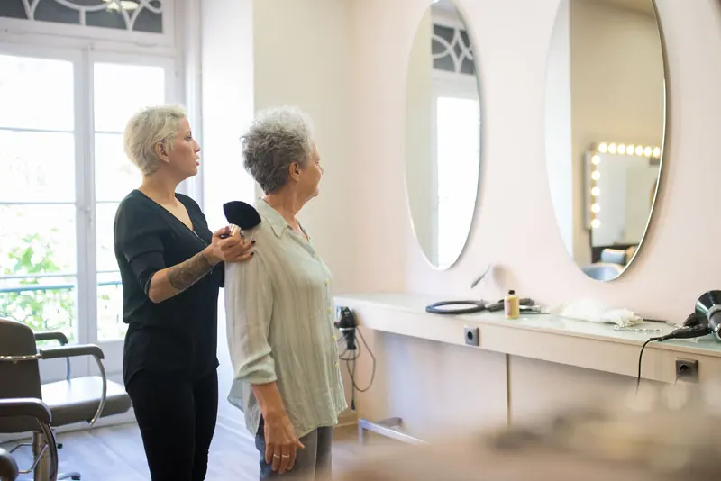 Hair stylist assisting a senior client in a modern salon with large mirrors.