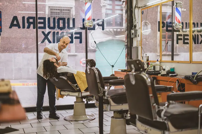 A barber expertly shaves a client's face in a classic barbershop setting.