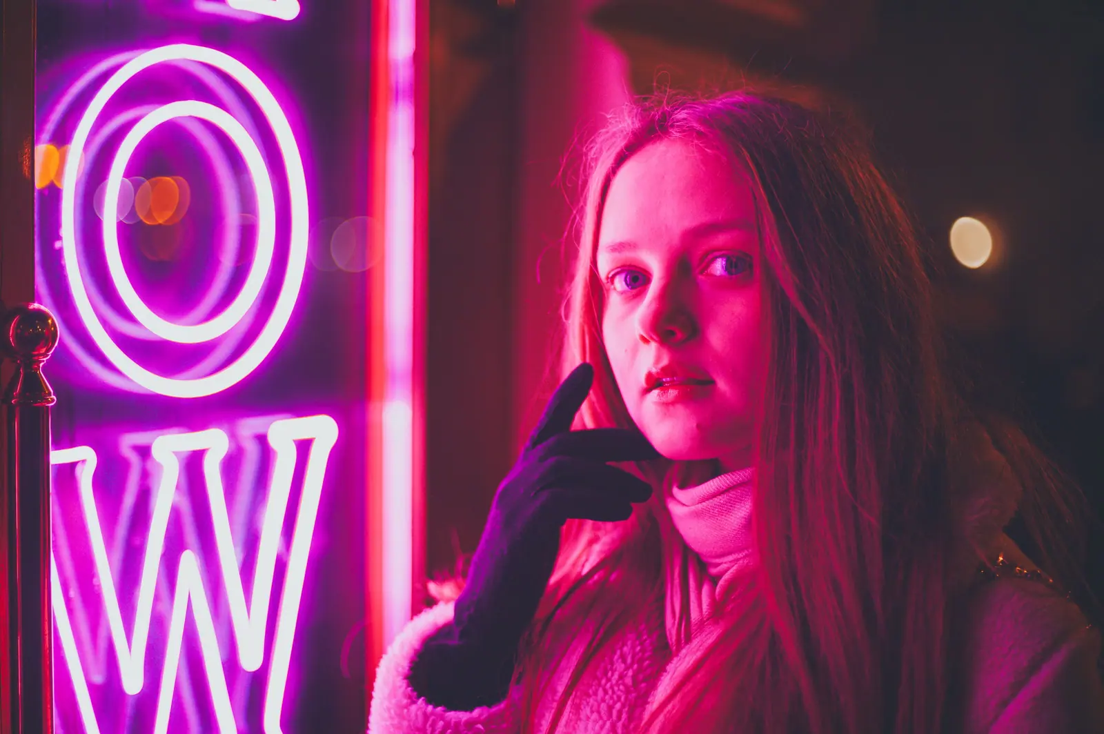 Woman in a soft lilac sweater lit by glowing pink neon letters