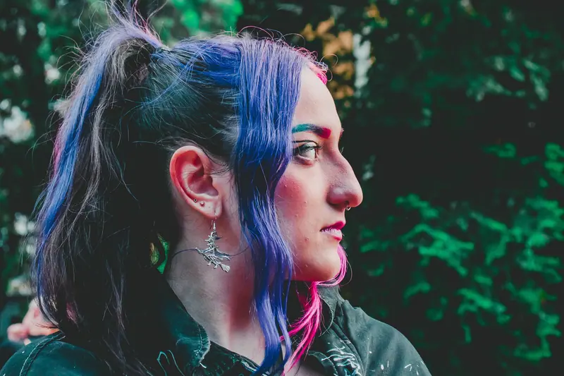 Profile portrait of a woman with vibrant hair and edgy style outdoors.