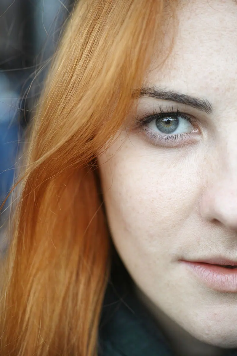 Close-up of glossy copper-gold hair falling across a freckled cheek
