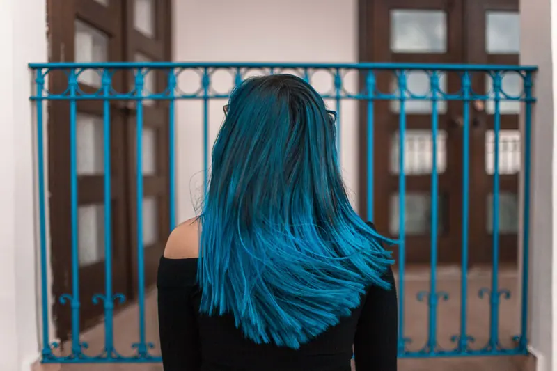Long blue-teal hair in front of an iron balcony
