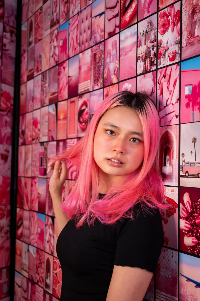 Vibrant portrait of a woman with pink hair against a colorful pink collage background.