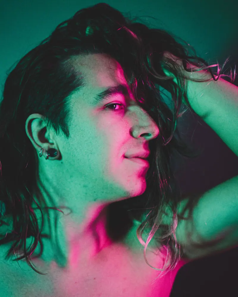 Man with long dark hair lit in pink and teal