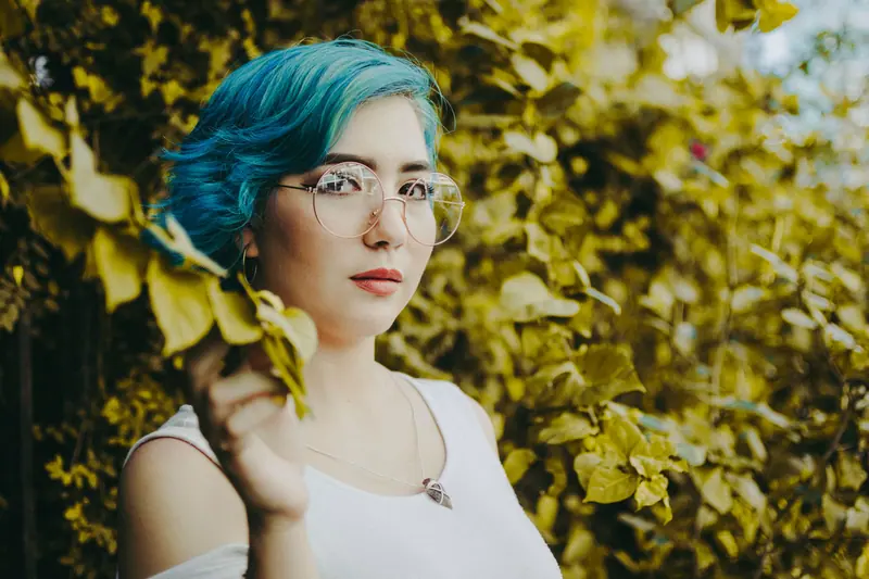 Blue hair and glasses among green leaves